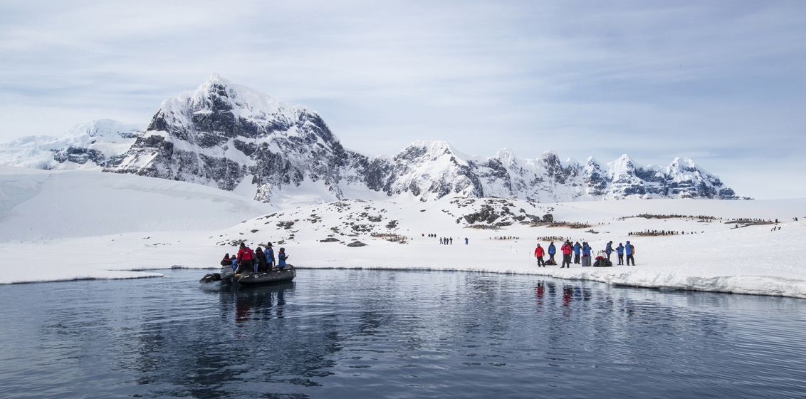 Passengers in orange jackets landing on Antarctic shore from Zodiac inflatable boats